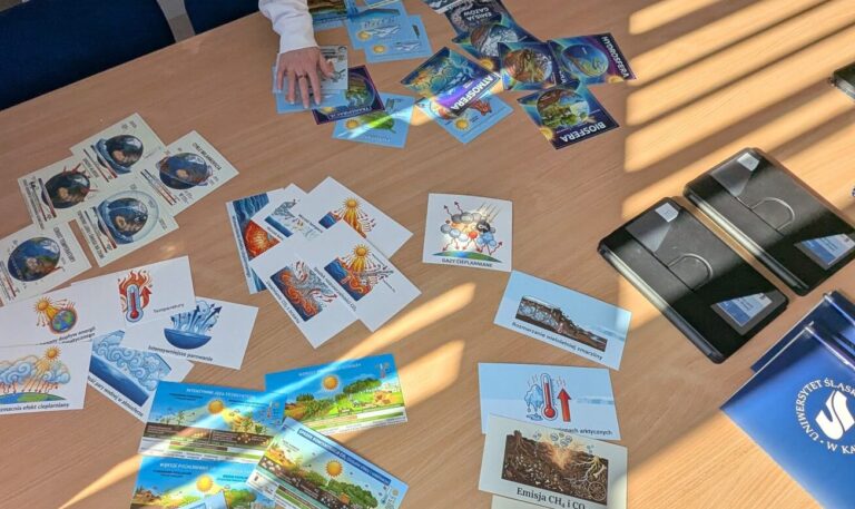 Uczestniczka warsztatów prezentuje na stole zestaw kart edukacyjnych i materiałów dotyczących zmian klimatu oraz procesów zachodzących w środowisku.